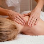 Therapist's hands massaging a person's upper back while they lie face down on a massage table.