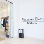 Massimo Dutti store entrance with white walls, glass door, and a shopper browsing clothing inside.