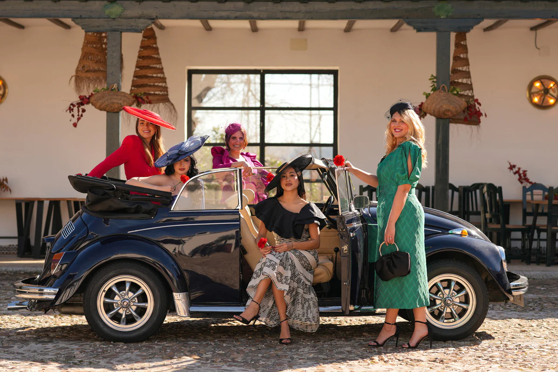 772931 - DNUE for Ladies 1 - Revista DeBelleza.Es Group of stylish women in vintage dresses and hats posing with a navy convertible in a sunny courtyard.