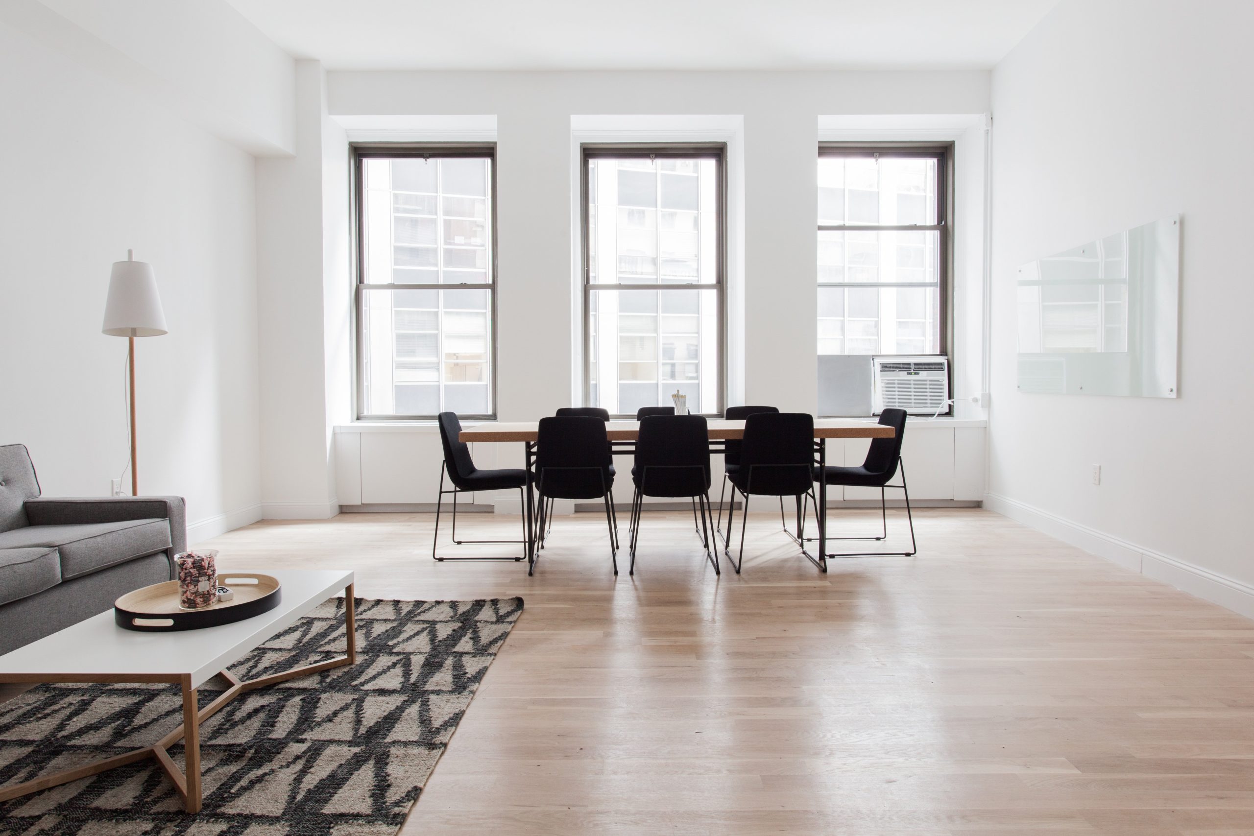 773889 - Marga Comas Interior Design - Revista DeBelleza.Es Bright modern dining room with a long wooden table and eight black chairs by large windows; a gray sofa on the left.
