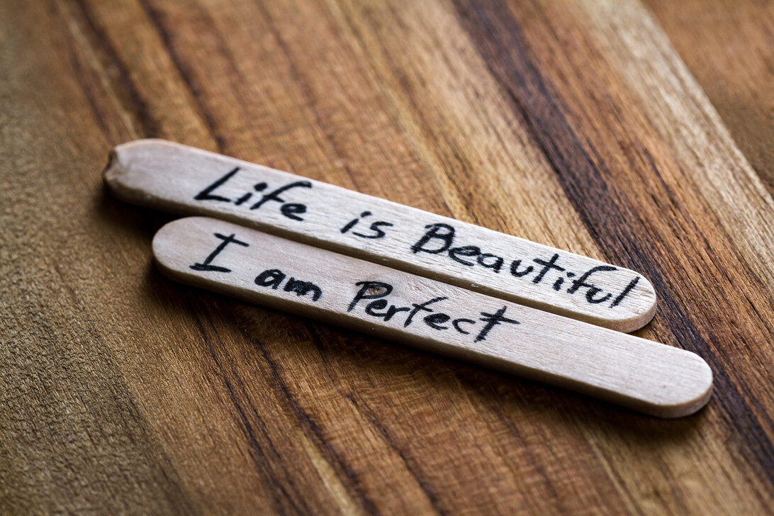 775539 Diana Isabel Carreazo - Revista DeBelleza.Es Two wooden sticks with handwritten inspirational phrases: 'Life is Beautiful' and 'I am Perfect' on a wooden surface.