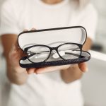 Person in a white shirt presenting an open glasses case containing black eyeglasses