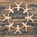 Eight wooden humanoid shapes arranged in a circle on a rustic wooden surface, symbolizing teamwork and community.