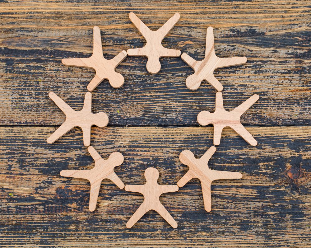 777564 - Institut Integratiu - Revista DeBelleza.Es Eight wooden humanoid shapes arranged in a circle on a rustic wooden surface, symbolizing teamwork and community.
