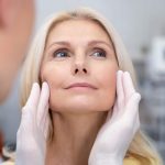 Medical professional in gloves gently palpating a woman's cheeks during a facial examination in a clinical setting